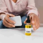 man with phone reaching for a CBD bottle