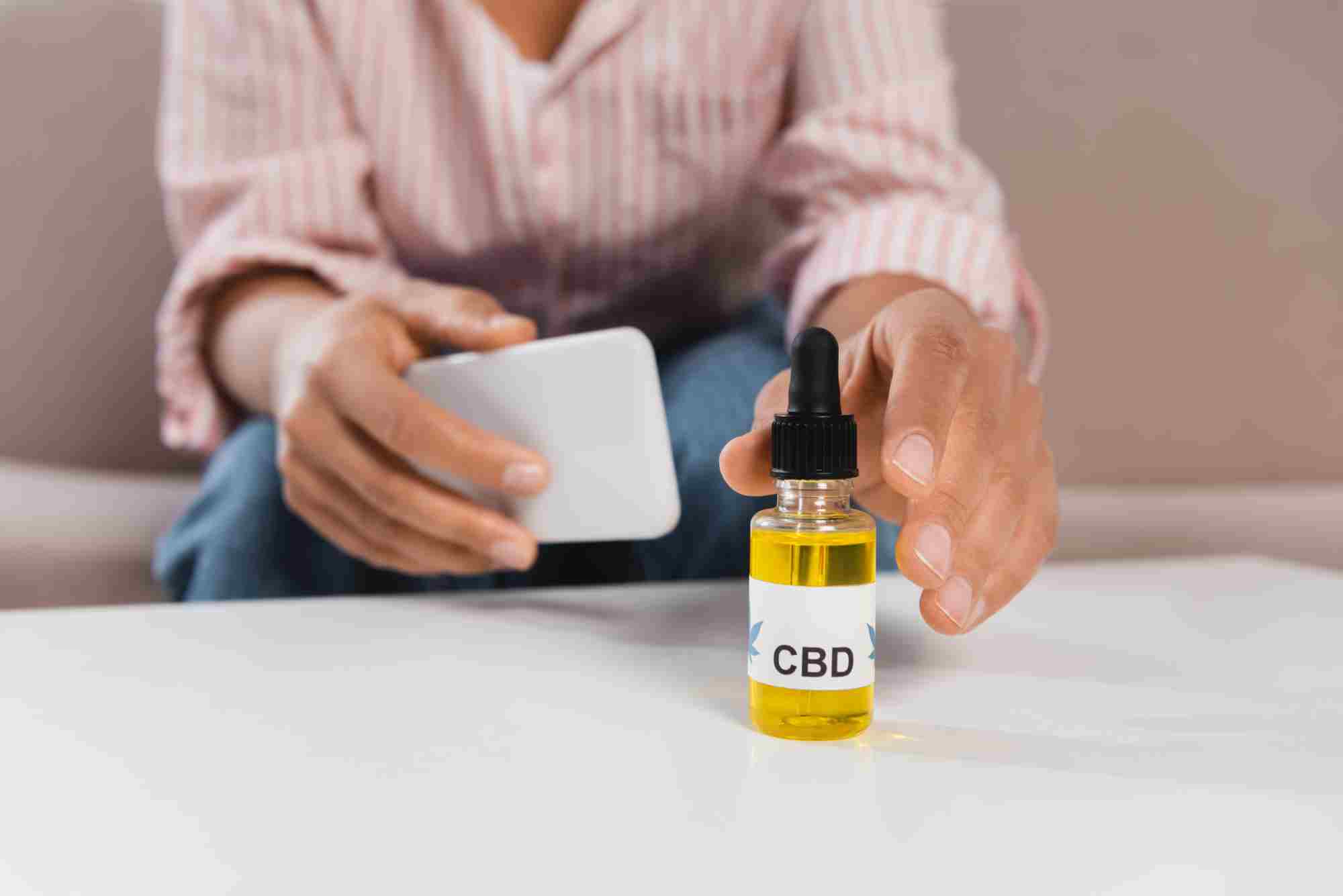 man with phone reaching for a CBD bottle